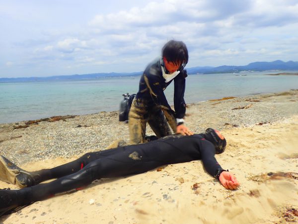 ダイビング事故が起こった時を想定し、気を失ったダイバーを海から引き揚げて砂浜でCPRを行う練習をしている