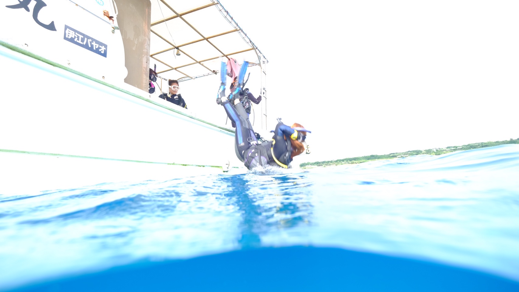 船のヘリに腰を掛けた器材を背負ったダイバーが、背中から海へ落ちる様子。